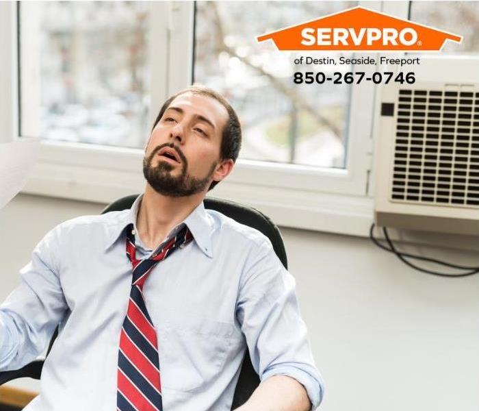 A person is cooling off in an office with a window-mounted air conditioning unit.
