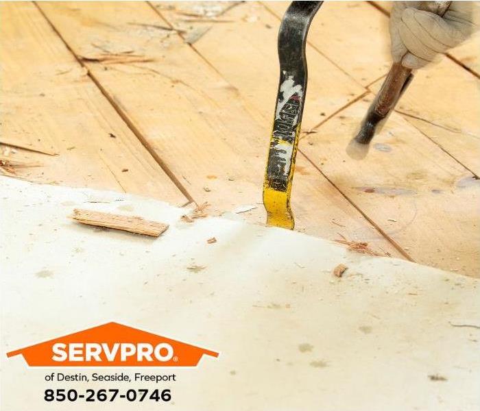 A damaged subfloor is removed with a crowbar and a hammer.